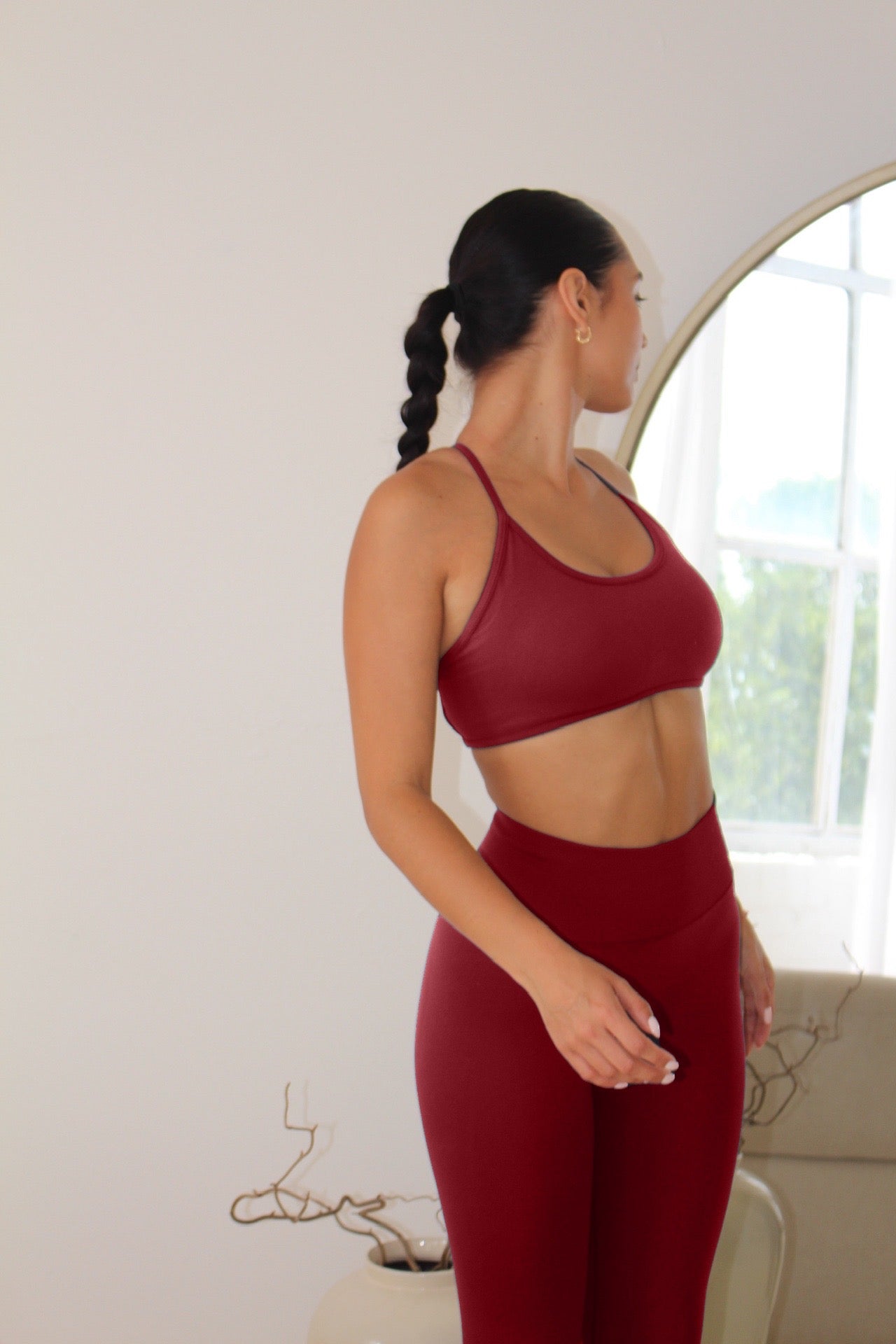Woman in profile wearing The Ilume Collection - Adjustable Cross Back Sports Bra, showcasing its fit and design in a bright, minimalist room.