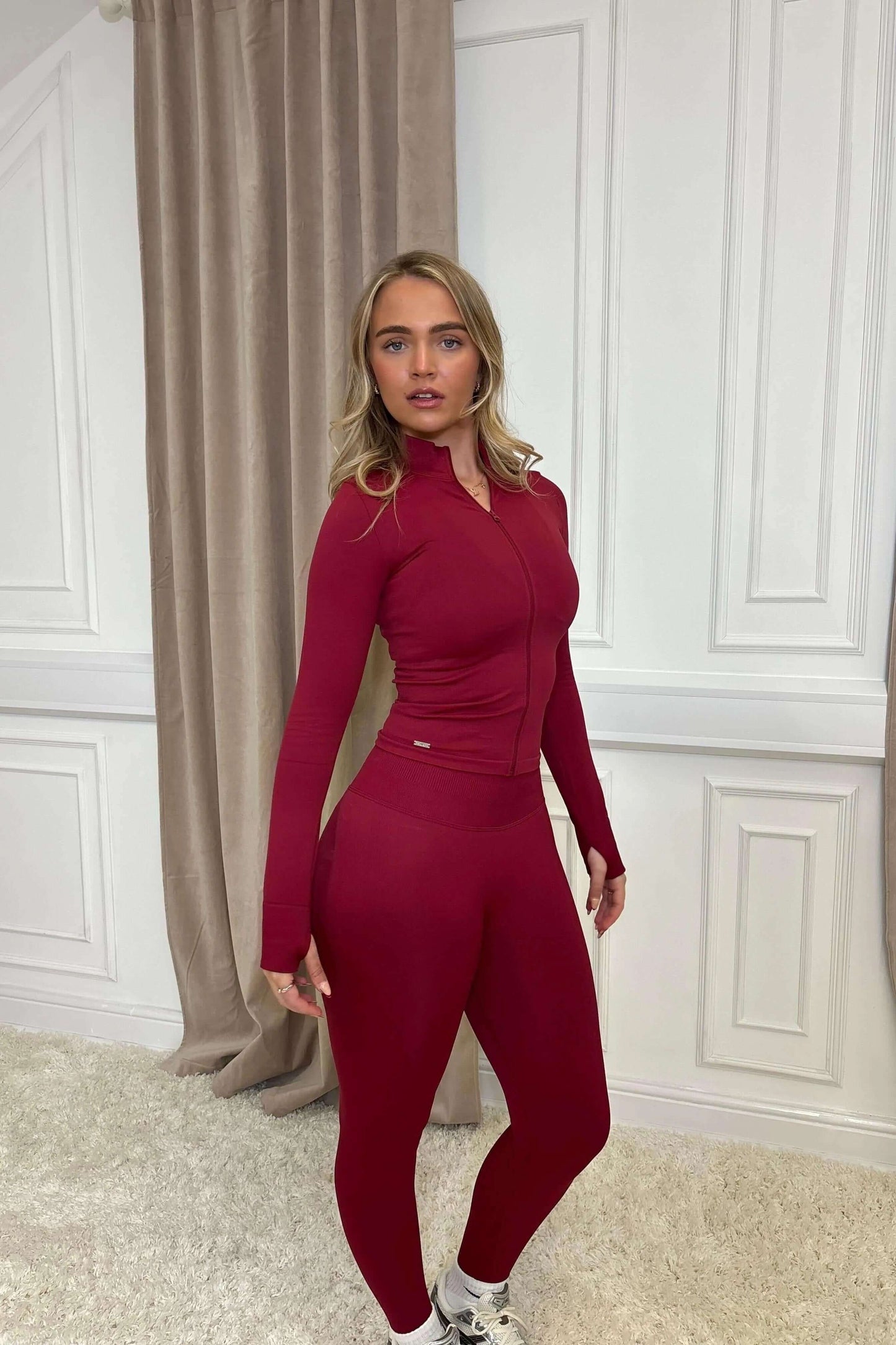 Young woman wearing The Empower Edge Collection - Scrunch Bum Gym Leggings, showcasing high-waisted fit, scrunch bum design, paired with a matching zip-up top and white shoes.