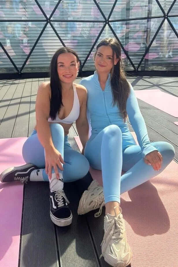 Two women in yoga poses wearing The Empower Edge Collection Gym Jacket, showcasing its form-fitting design in a geodesic-style studio with mural artwork.