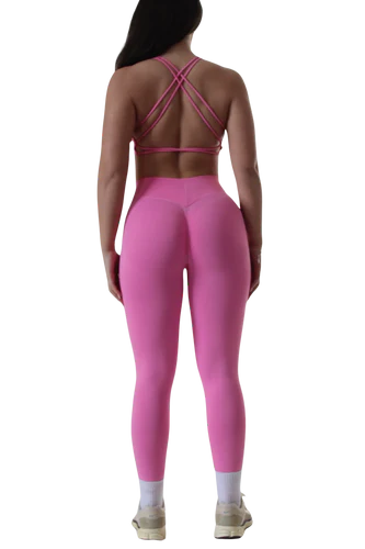 A woman in pink leggings and a matching top is standing, showcasing her activewear outfit. The image focuses on her back and legs.