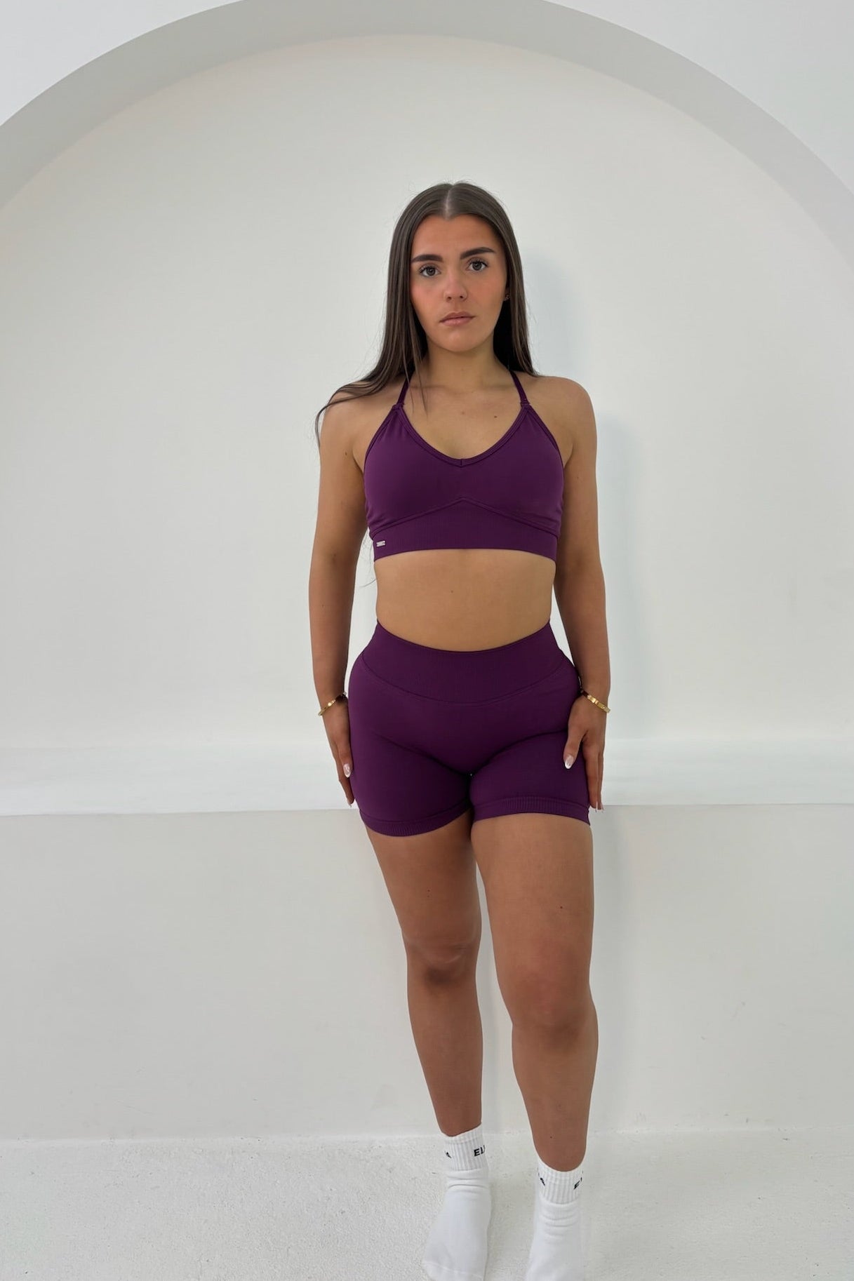Young woman wearing The Elena Noor Collection - Sculpting Scrunch Bum Shorts, showcasing a flattering fit in a minimalist setting.