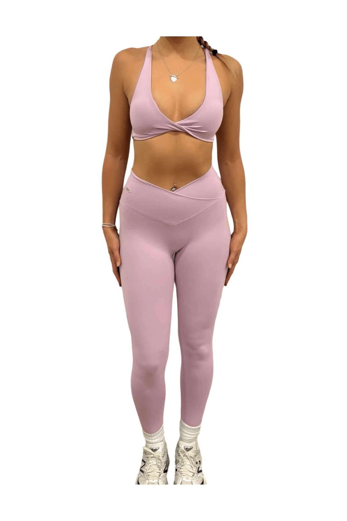 Woman modeling Pilates Reformer Collection high-waisted wrap front leggings, showcasing fit and support, paired with white sneakers and a necklace for gym readiness.