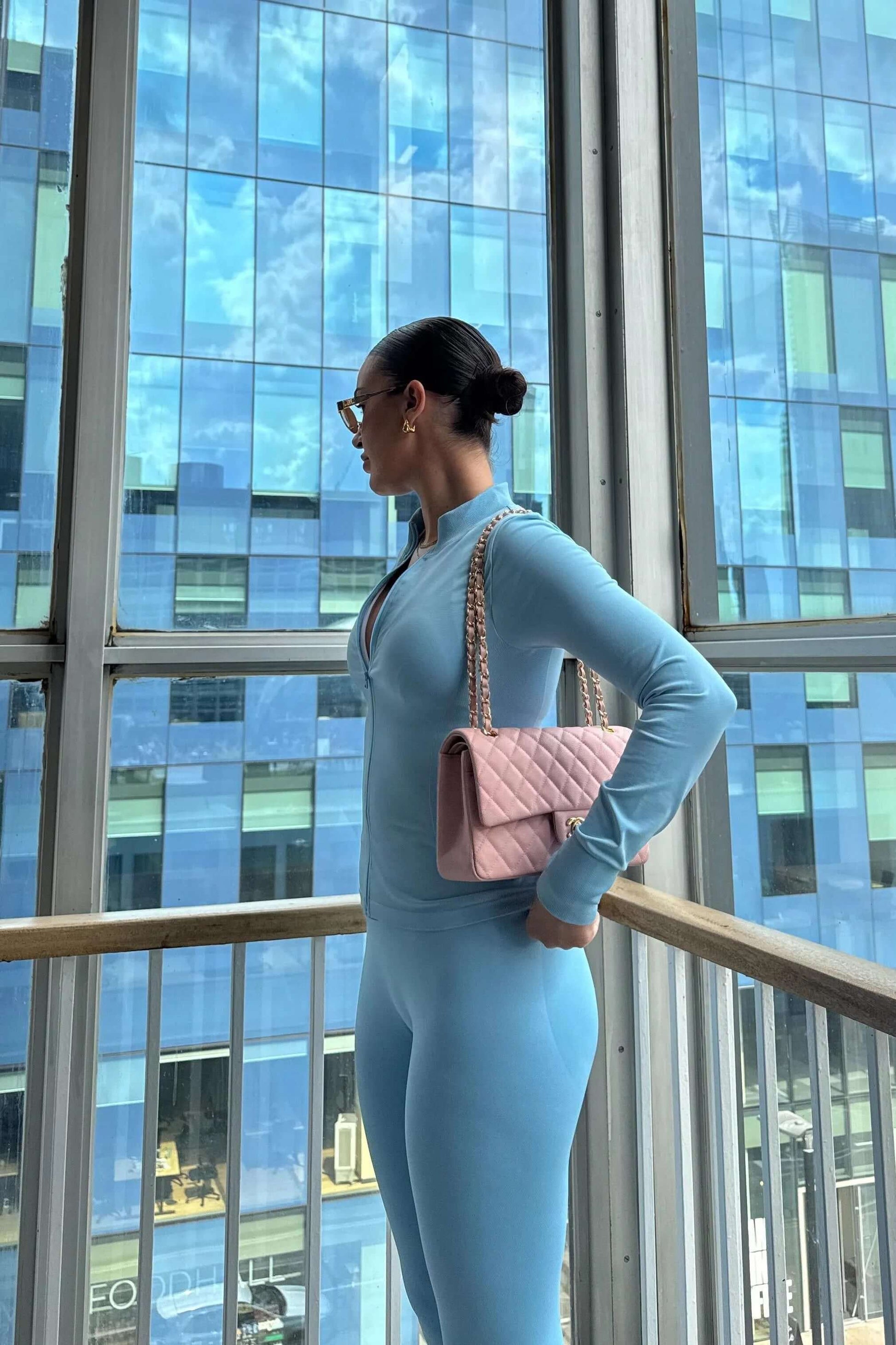 Person wearing the 3 Piece Set Edge Jacket, Leggings, and Ilume Top in Blue stands by a window, highlighting the set's form-fitting and coordinated design.
