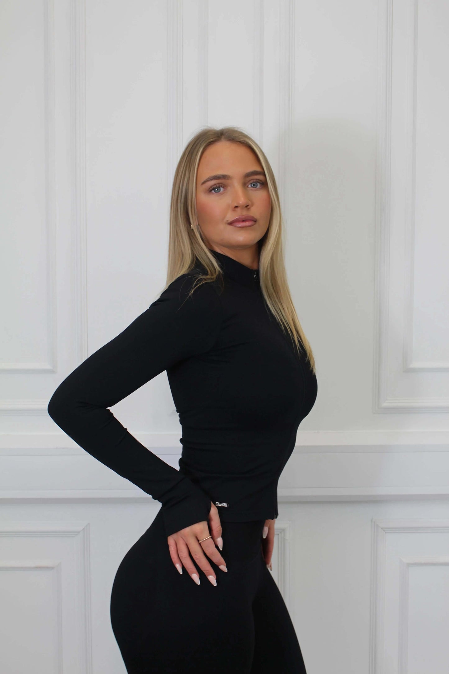 Young woman in profile wearing The Empower Edge Collection Gym Jacket, showcasing its form-fitting design with thumbholes and high-waisted leggings, highlighting luxury and comfort.