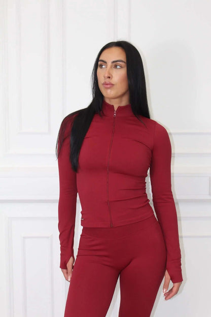 Person in The Empower Edge Collection Gym Jacket, form-fitting burgundy zip-up with matching leggings, showcasing luxury and comfort for an elevated workout experience.