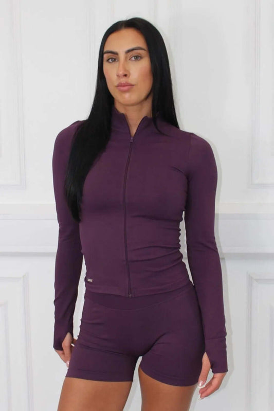 A woman models The Empower Edge Collection - Gym Jacket, showcasing its fitted design, long sleeves with thumbholes, and luxurious stretch material for workout comfort.