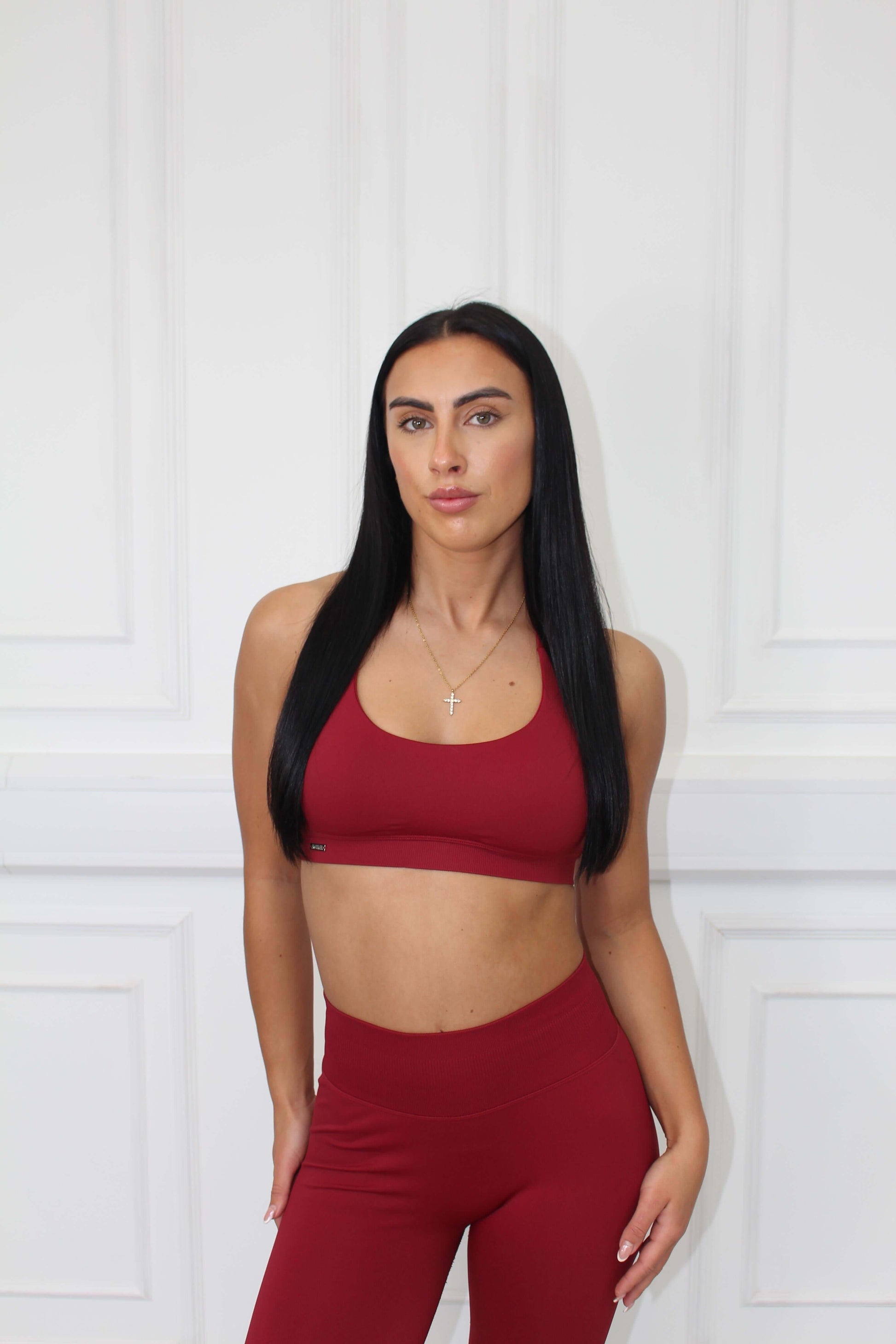 A young woman models The Edge Collection Gym Bra, showcasing its personalized fit and curve control against a white paneled wall.