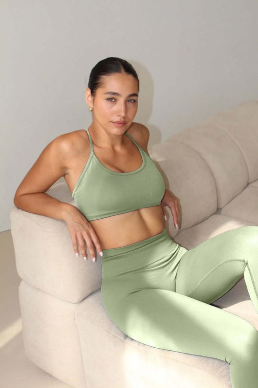 A woman reclines on a sofa wearing The Ilume Collection - Adjustable Cross Back Sports Bra, showcasing its sleek, supportive design and adjustable cross-back straps.