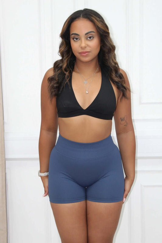 Young woman wearing The Ilume Collection - Halter Low Cut Gym Bra, showcasing its flattering low-cut design and supportive fit, paired with high-waisted athletic shorts.