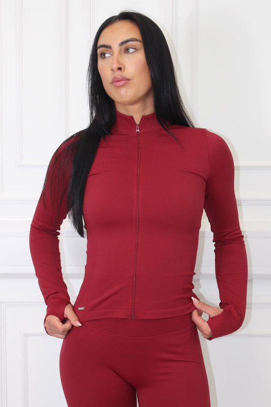 The Empower Edge Collection - Gym Jacket features a zip-up design with a snug fit, modeled by a woman in a red outfit.