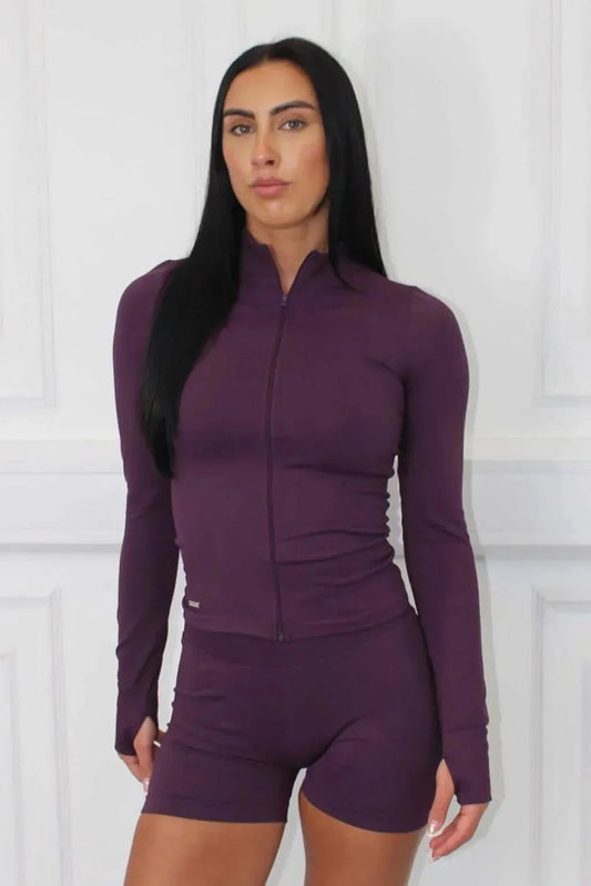 Model in The Empower Edge Collection Gym Jacket, a form-fitting zip-front top with thumbholes, paired with matching high-waisted bike shorts, showcasing luxury athleisure wear.